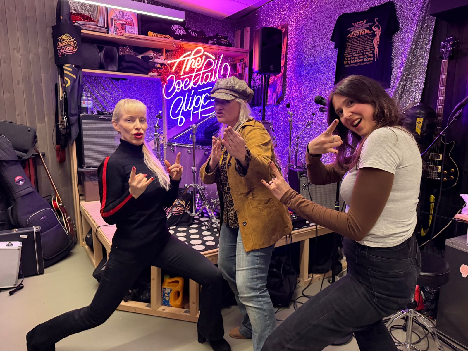 Stine, Astrid og Sandra fra The Cocktail Slippers poserer foran neonskiltet i øvingslokalet